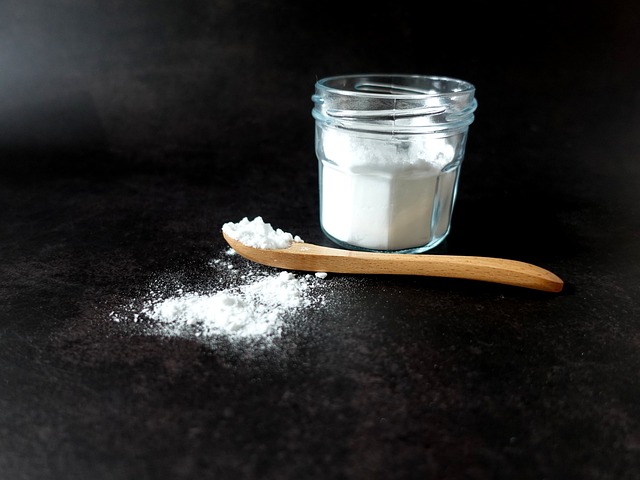 Baking soda in a glass jar alongside a wooden spoon full of baking soda