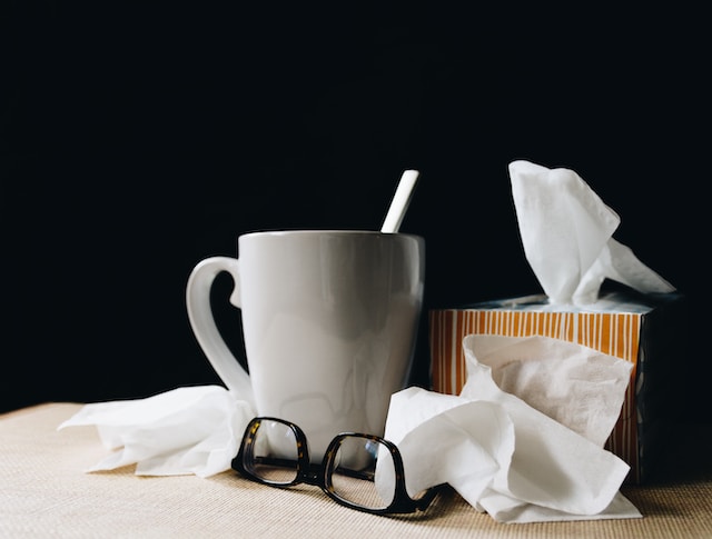 Glasses, a mug, and a tissue box on a table. Beside the tissue box is used tissues