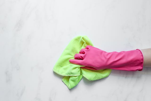 Person with pink gloves cleaning a table with a green rag